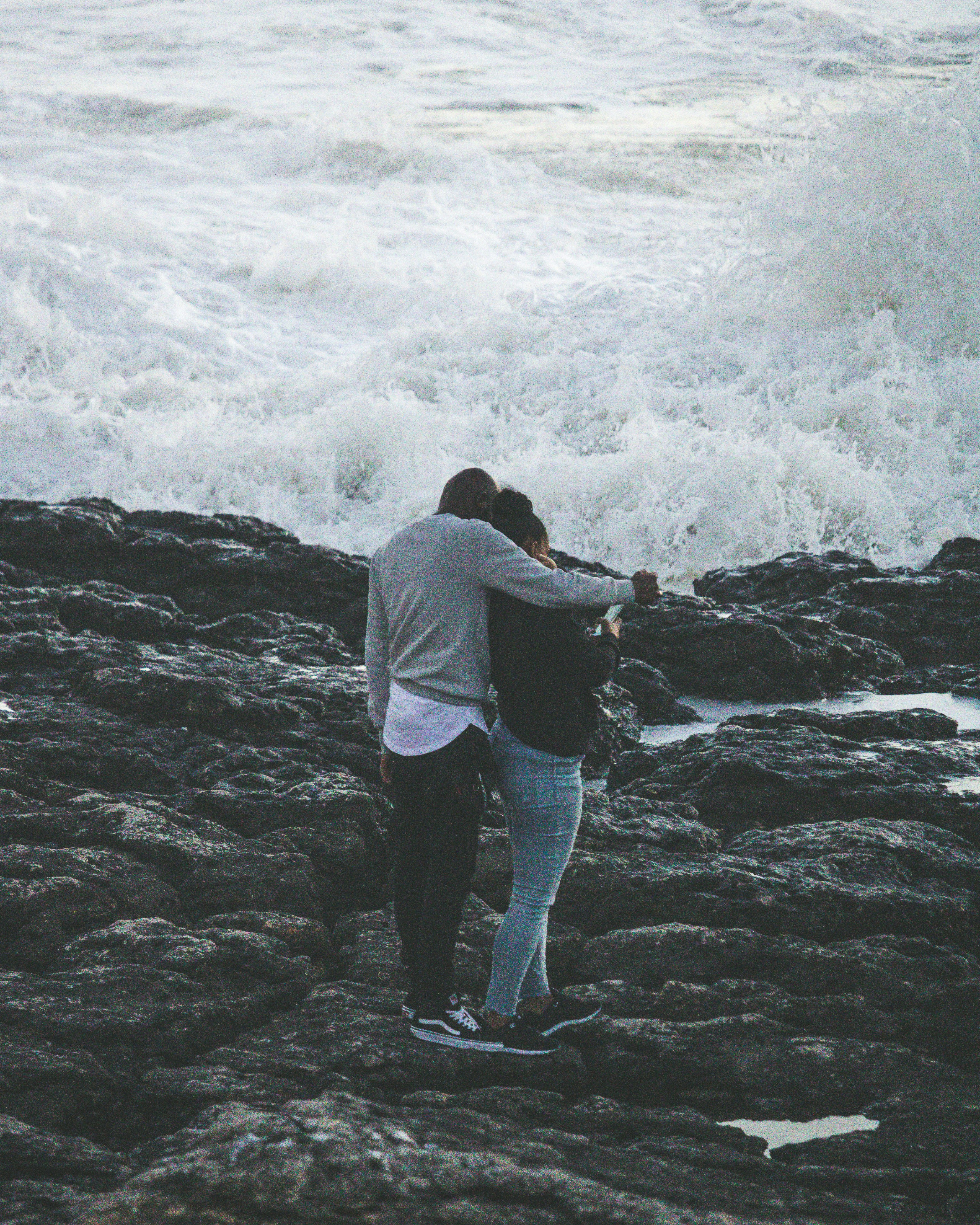 man and woman on rock near beach talking photo